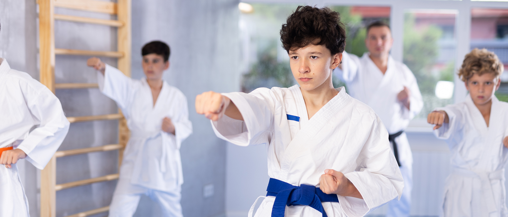 Willing junior boy wearing kimono training karate techniques in group during workout session